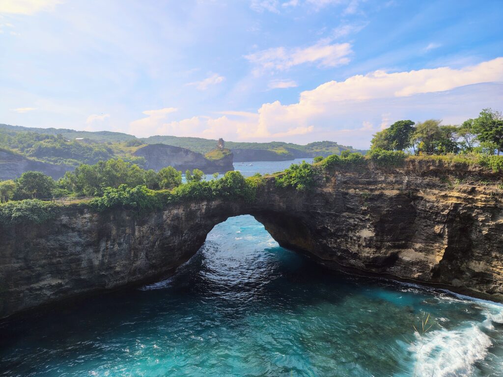 A breathtaking view of Broken Beach on Nusa Penida, Indonesia, showing a natural limestone archway over turquoise ocean waters. This scenic landscape from a travel journey highlights the dramatic cliffs and vibrant blue sea characteristic of the Balinese islands.